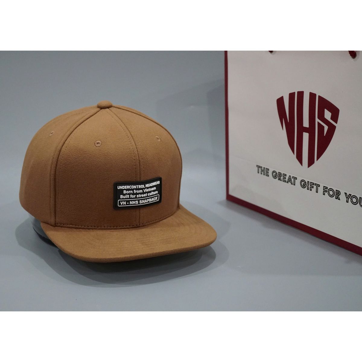 Mũ snapback da lộn NHS bên cạnh túi quà THE GREAT GIFT FOR YOU